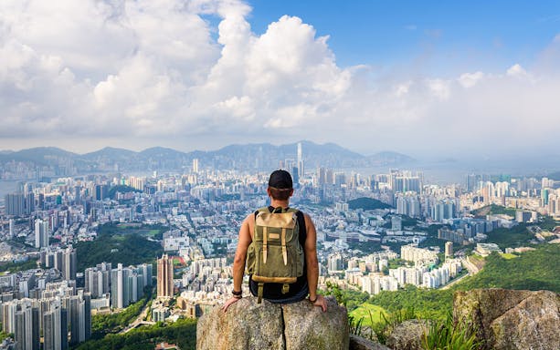 Traveler overlooking Hong Kong skyline from a mountain viewpoint.
