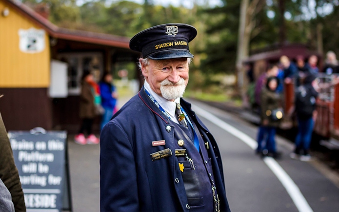 Station Master in uniform smiling on the platform during a Puffing Billy tour.