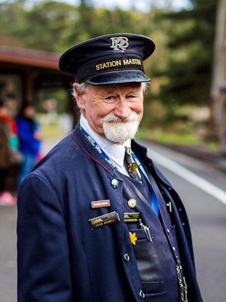 Station Master in uniform smiling on the platform during a Puffing Billy tour.