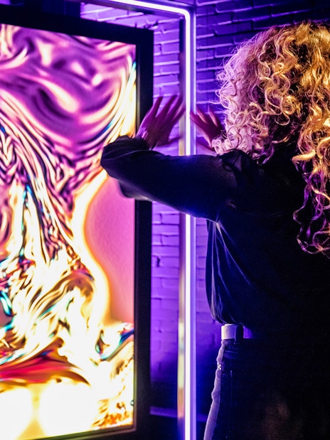 Person interacting with vibrant digital art at AMAZE Amsterdam Immersive Experience.
