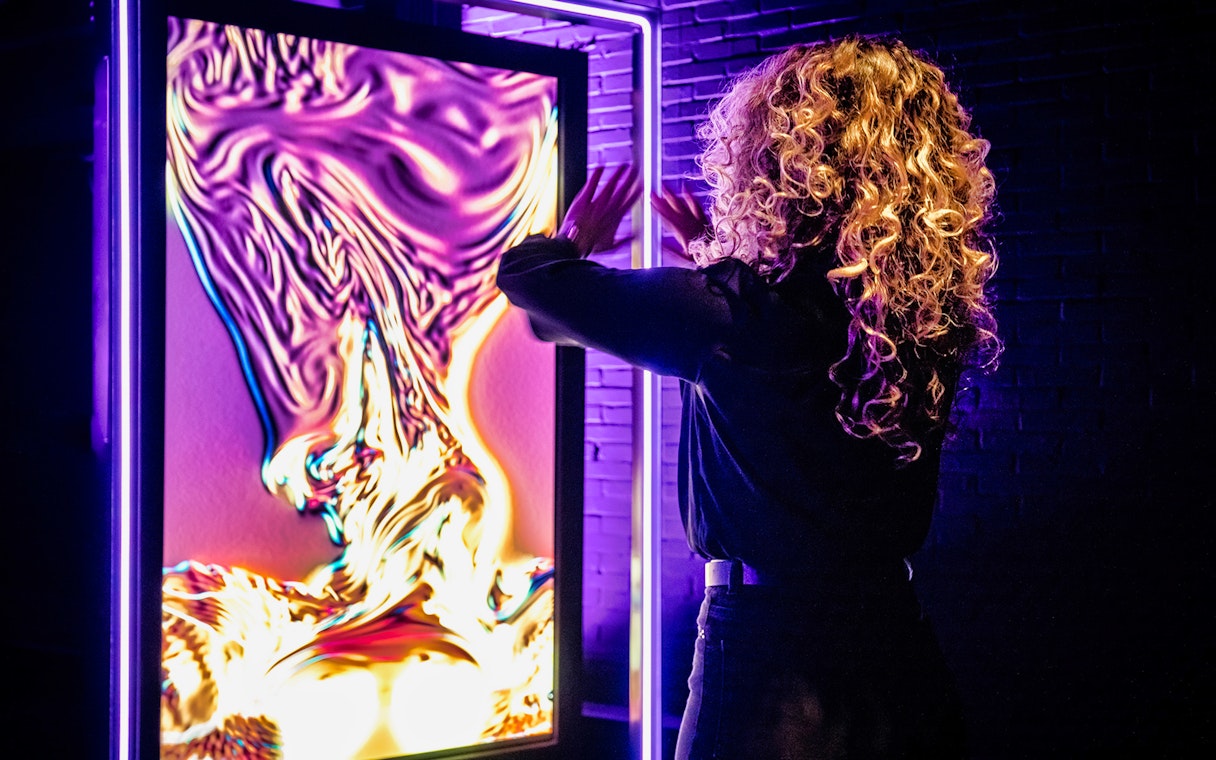 Person interacting with vibrant digital art at AMAZE Amsterdam Immersive Experience.