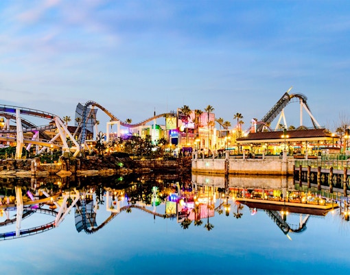 Roller coasters and vibrant lights at Universal Studios Japan reflected in water.
