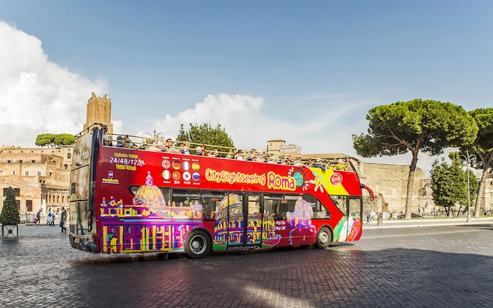 Open-top sightseeing bus in Rome near ancient ruins.