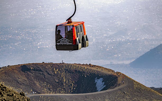 Cable car ascending Mount Etna with volcanic landscape in the background.