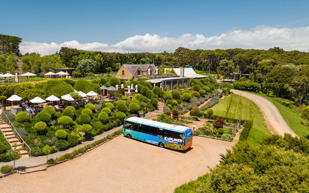 Western Explorer Hop-On Hop-Off Bus at a scenic garden estate with outdoor seating.