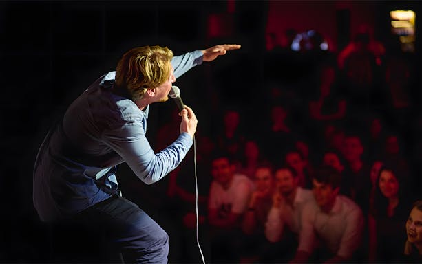 Comedian performing on stage at The Comedy Embassy with audience laughing.