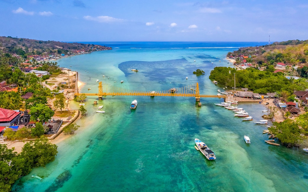 Yellow Bridge connecting Nusa Ceningan and Nusa Lembongan over turquoise waters with boats nearby.