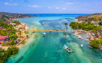 Yellow Bridge connecting Nusa Ceningan and Nusa Lembongan over turquoise waters with boats nearby.