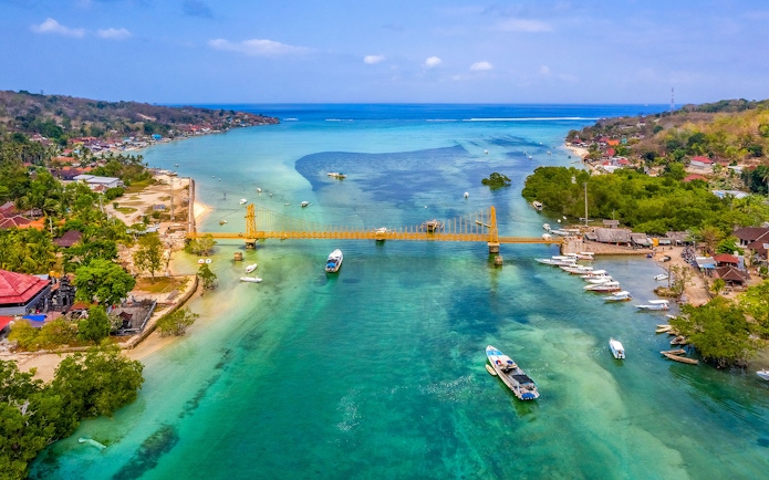 Yellow Bridge connecting Nusa Ceningan and Nusa Lembongan over turquoise waters with boats nearby.