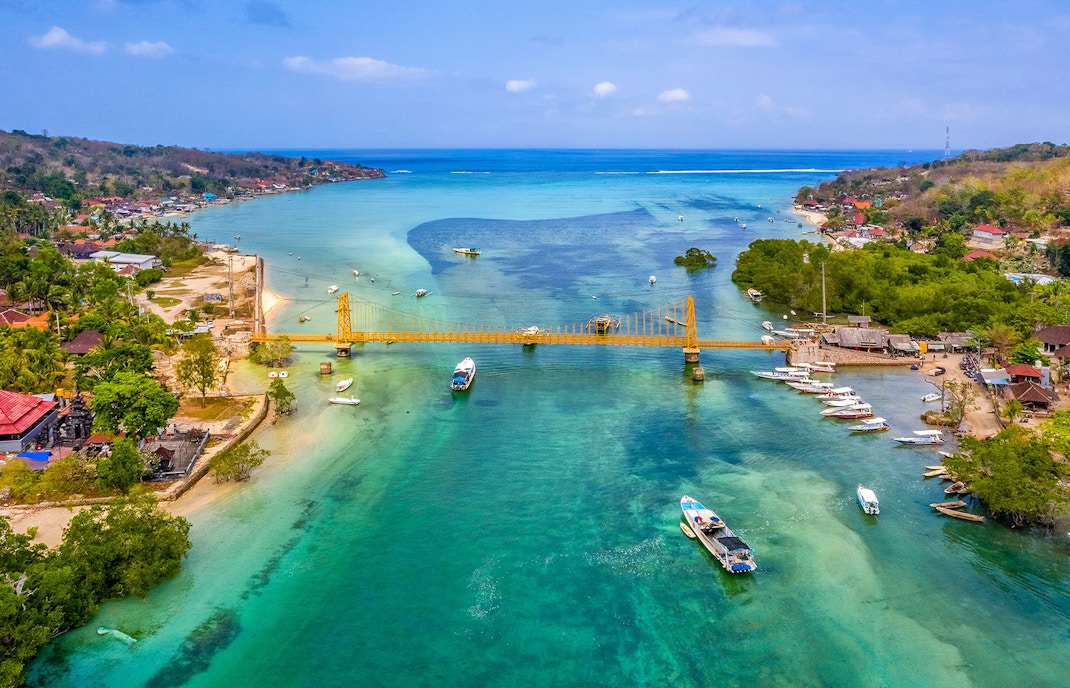 Yellow Bridge connecting Nusa Ceningan and Nusa Lembongan over turquoise waters with boats nearby.