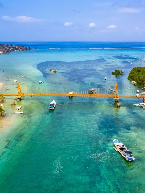Yellow Bridge connecting Nusa Ceningan and Nusa Lembongan over turquoise waters with boats nearby.