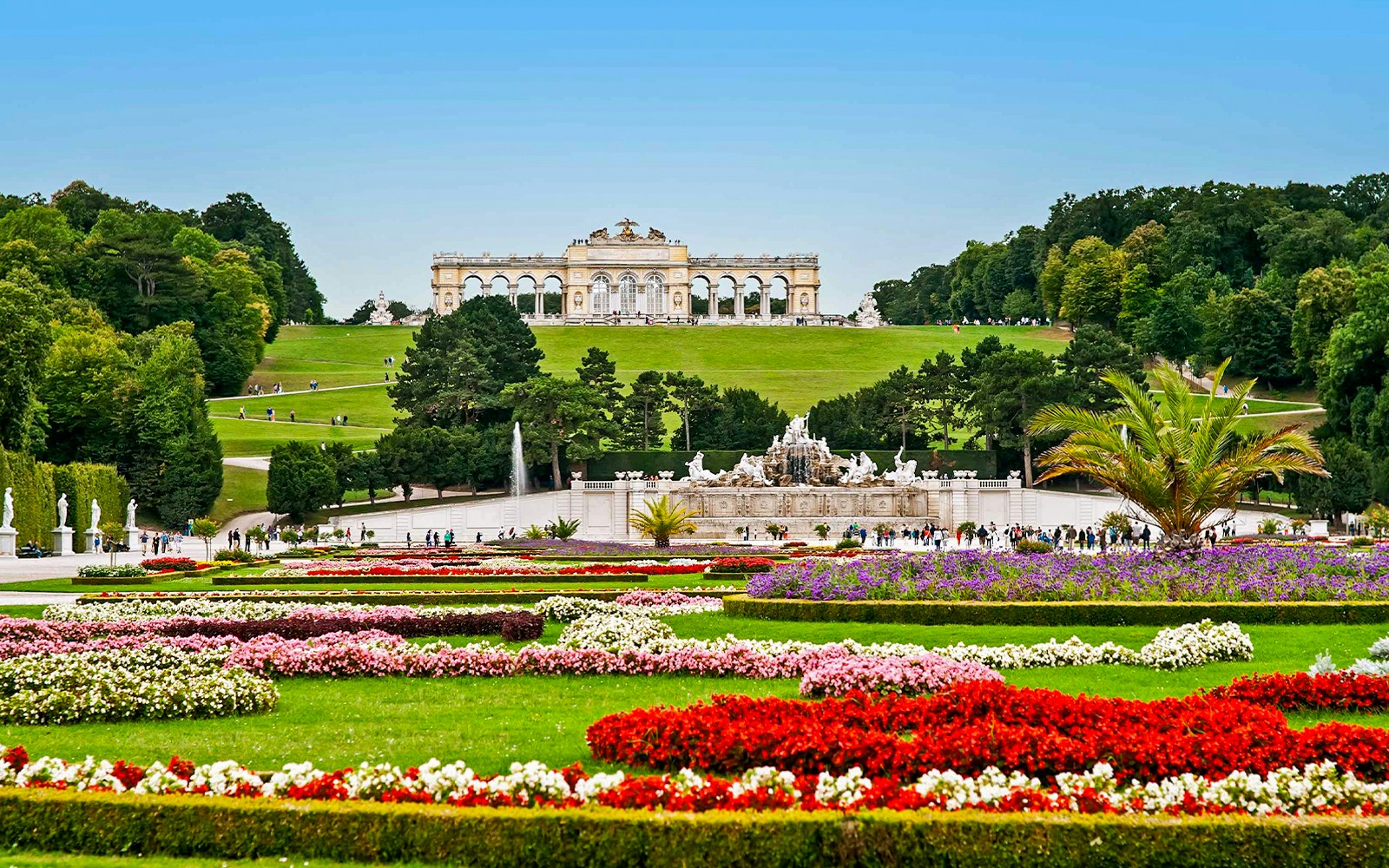Schönbrunn Palace gardens with Gloriette in Vienna, featuring colorful flower beds and fountains.