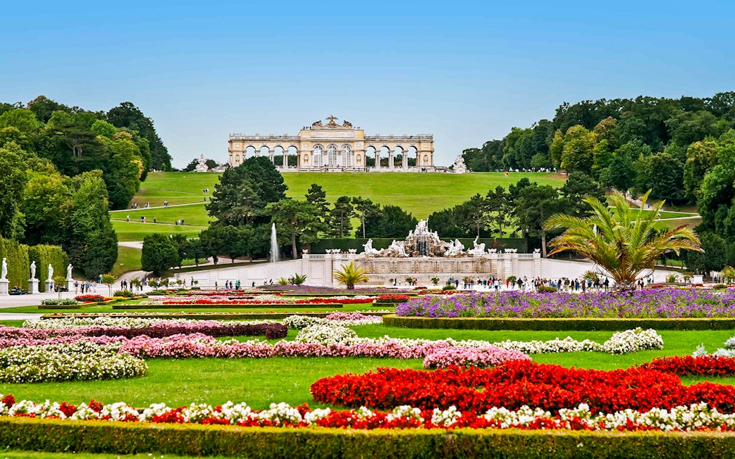Schönbrunn Palace gardens with Gloriette in Vienna, featuring colorful flower beds and fountains.