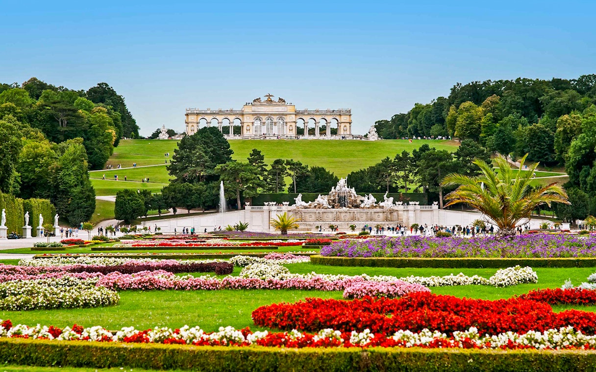 Schönbrunn Palace gardens with Gloriette in Vienna, featuring colorful flower beds and fountains.