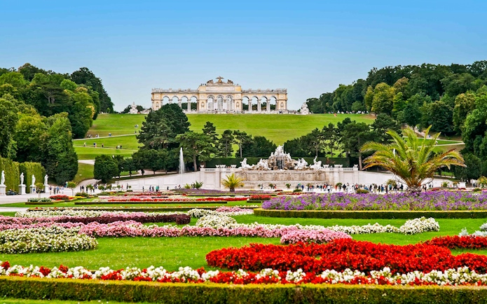 Schönbrunn Palace gardens with Gloriette in Vienna, featuring colorful flower beds and fountains.