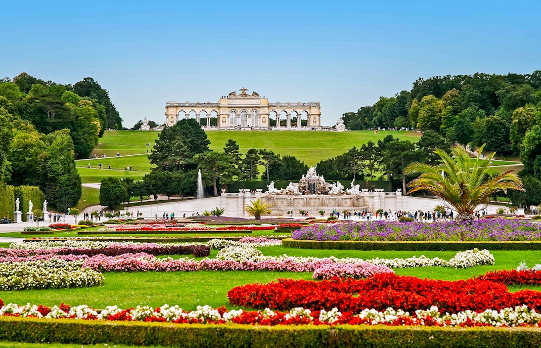 Schönbrunn Palace gardens with Gloriette in Vienna, featuring colorful flower beds and fountains.