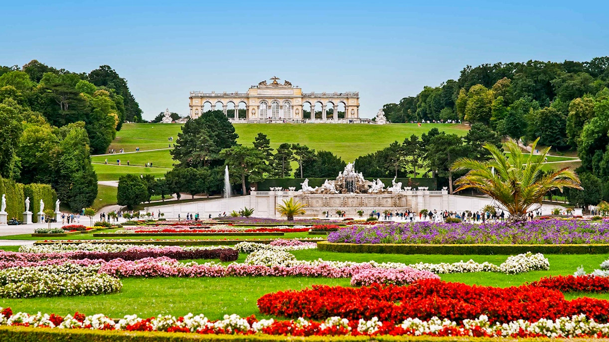 Schönbrunn Palace gardens with Gloriette in Vienna, featuring colorful flower beds and fountains.