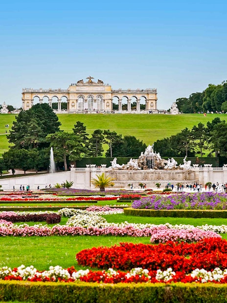 Schönbrunn Palace gardens with Gloriette in Vienna, featuring colorful flower beds and fountains.