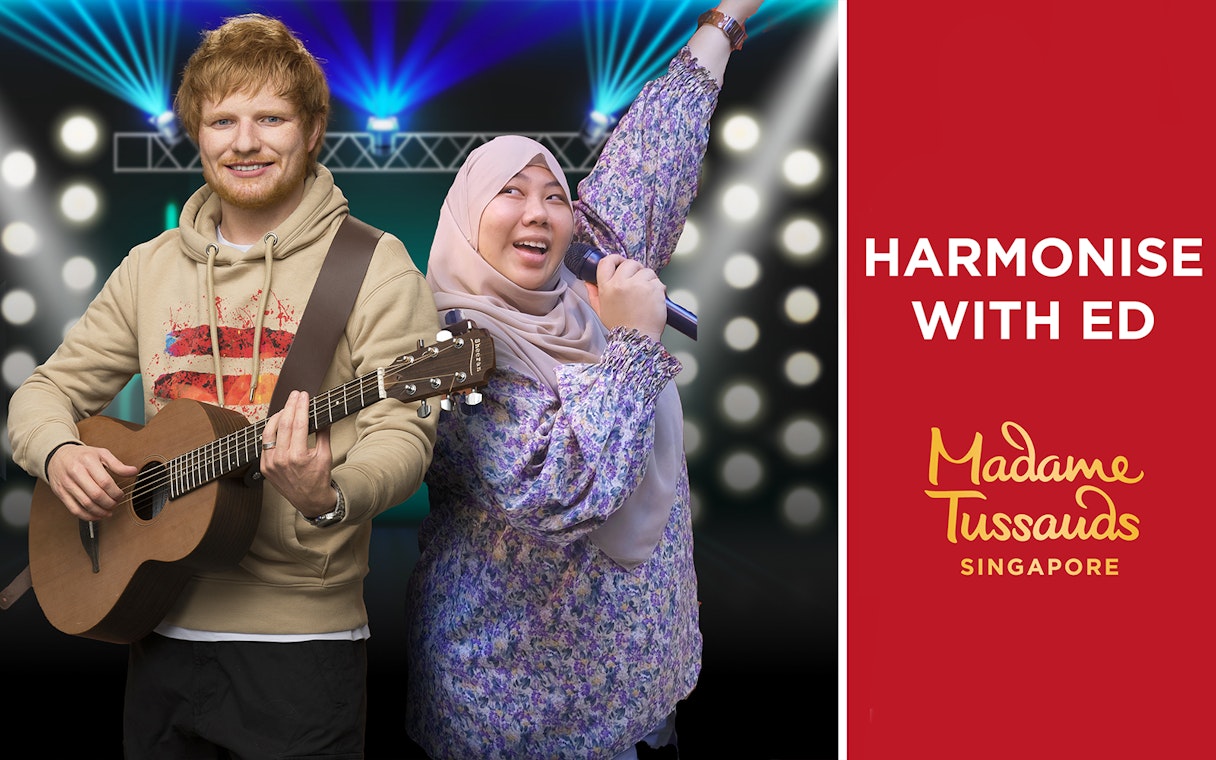 Wax figure of a musician with a guitar and a visitor singing at Madame Tussauds Singapore.