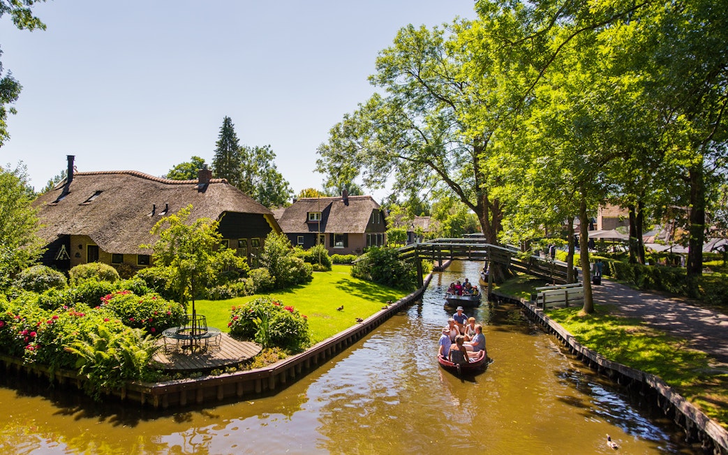 Canal boat tour in Giethoorn with thatched cottages and lush greenery.