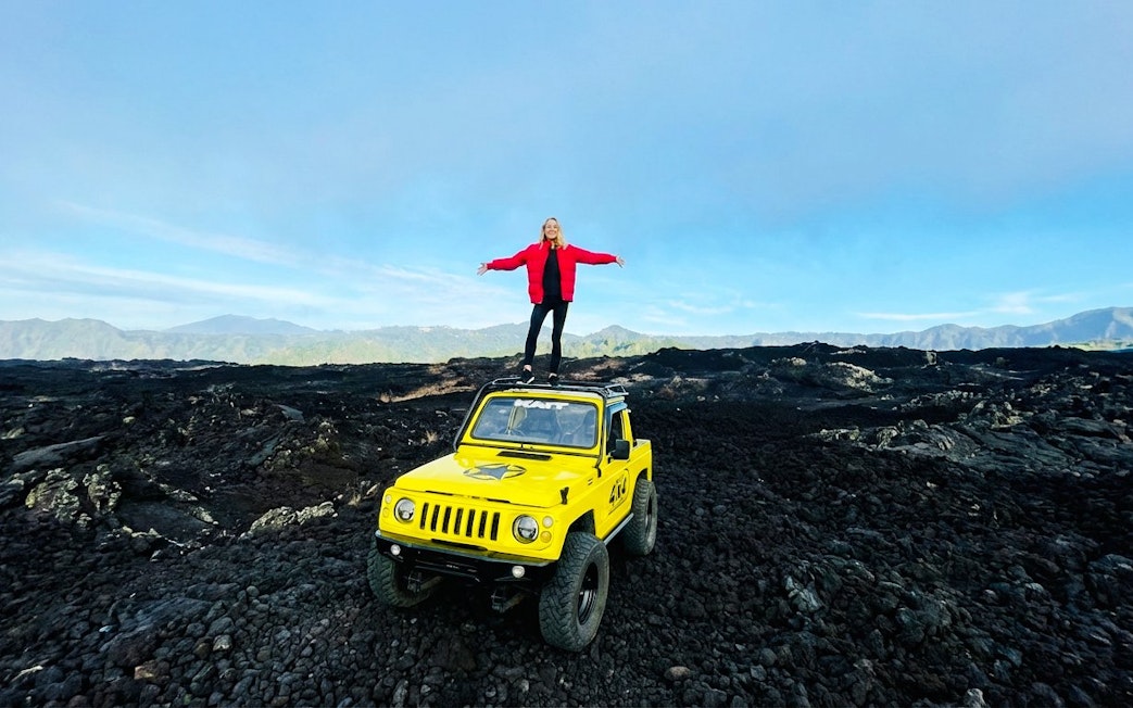 Person standing on a yellow jeep amidst black lava fields in Bali.
