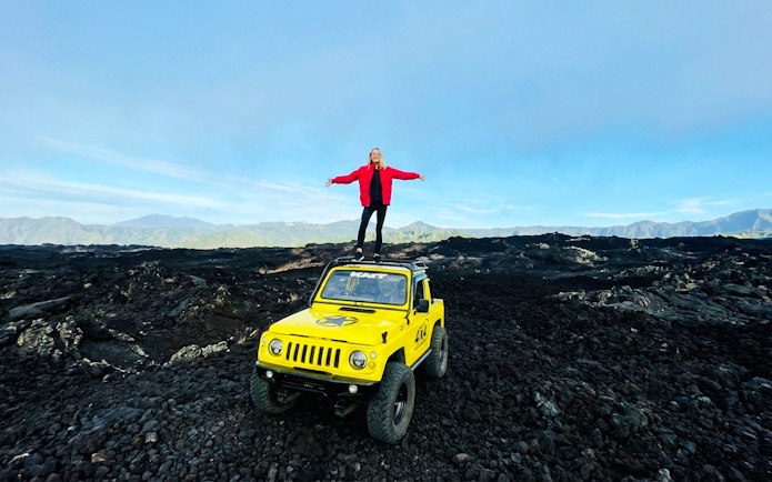 Person standing on a yellow jeep amidst black lava fields in Bali.