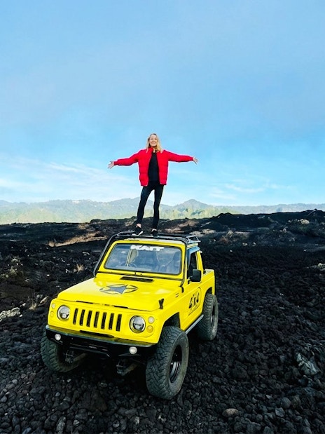 Person standing on a yellow jeep amidst black lava fields in Bali.