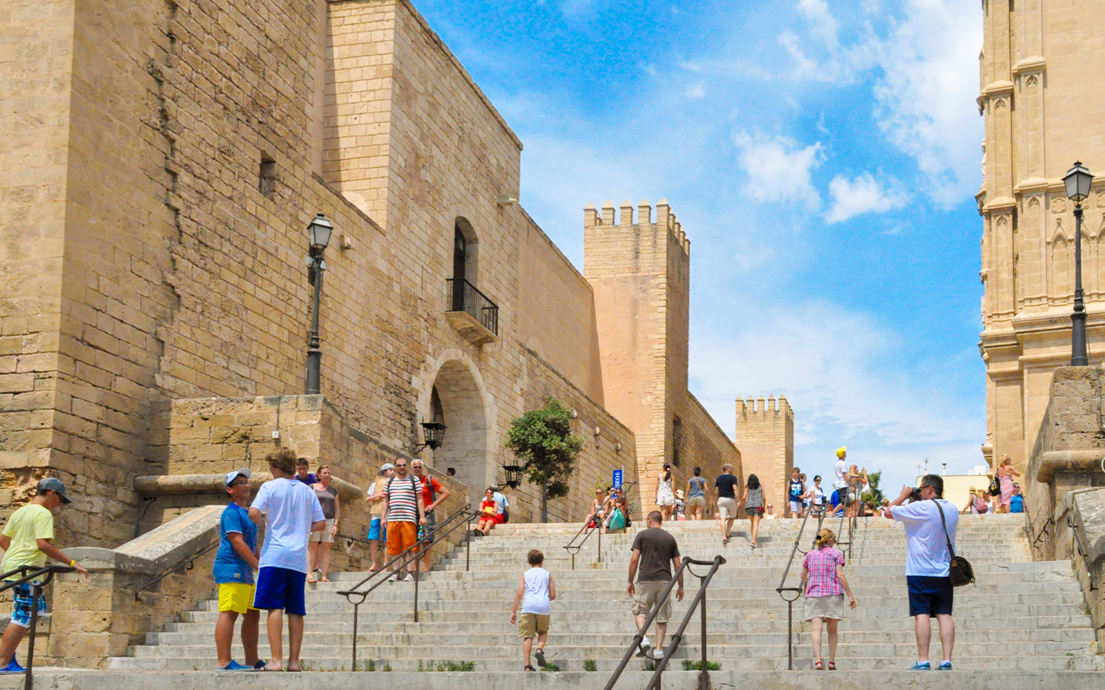 Visitors walking up stone steps in Palma Old Town, Mallorca, with historic buildings in view.