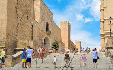 Visitors walking up stone steps in Palma Old Town, Mallorca, with historic buildings in view.