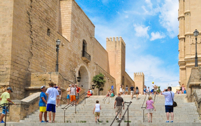 Visitors walking up stone steps in Palma Old Town, Mallorca, with historic buildings in view.