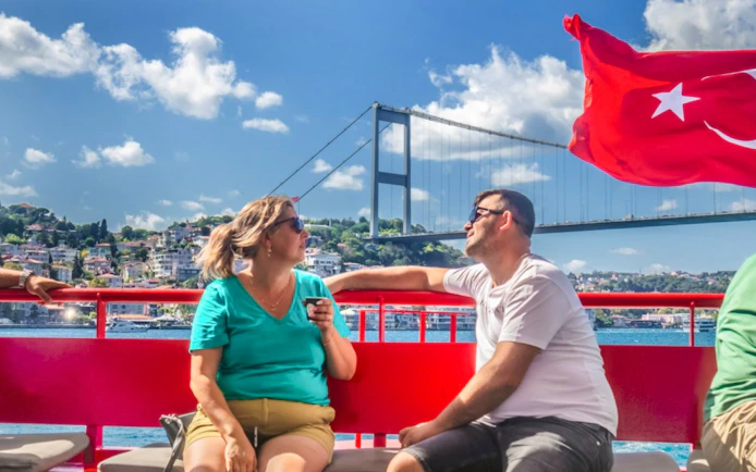 Guests on Bosphorus cruise with bridge and Turkish flag in background.