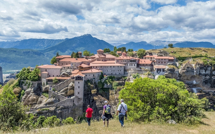 Guests hiking towards Meteora monastery with mountain backdrop.