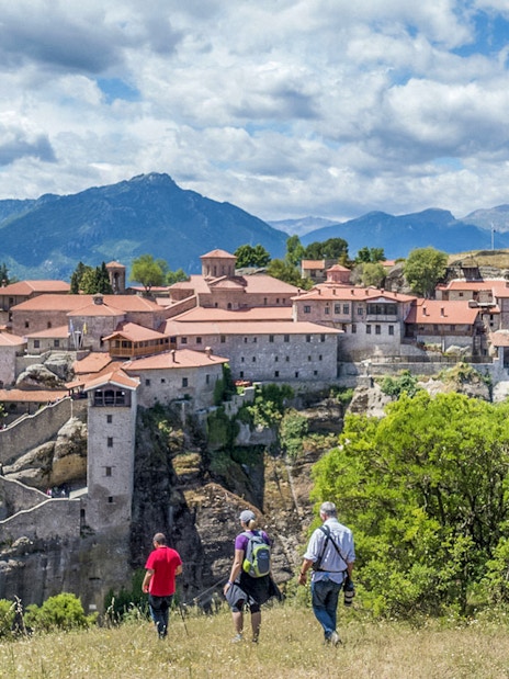 Guests hiking towards Meteora monastery with mountain backdrop.