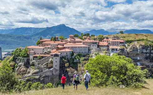 Guests hiking towards Meteora monastery with mountain backdrop.