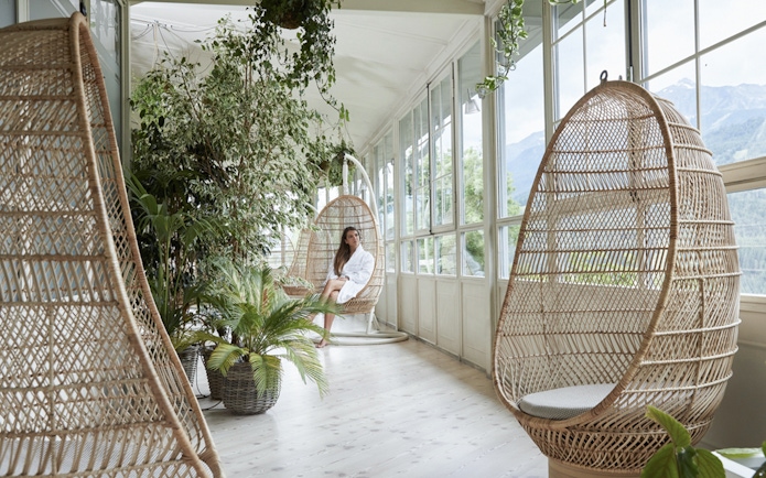 Woman relaxing in a wicker chair at QC Terme Bagni Nuovi di Bormio spa with mountain view.