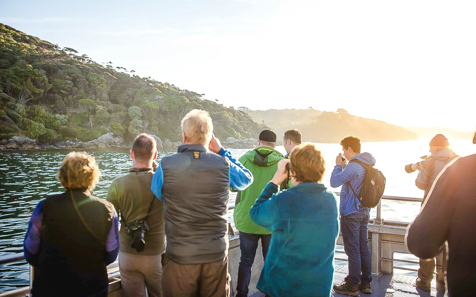 Tourists on a boat at sunset on Stewart Island watching the coastline and sky.