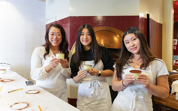 Participants holding tiramisu in a Rome cooking class kitchen.