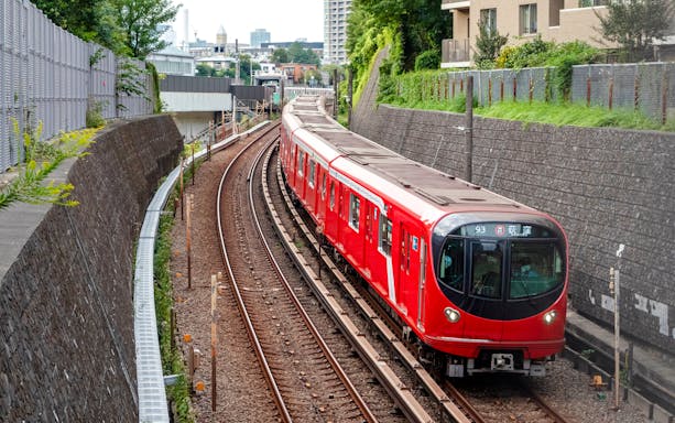 Tokyo Metro 2000 series train on Marunouchi Line tracks, surrounded by urban greenery.
