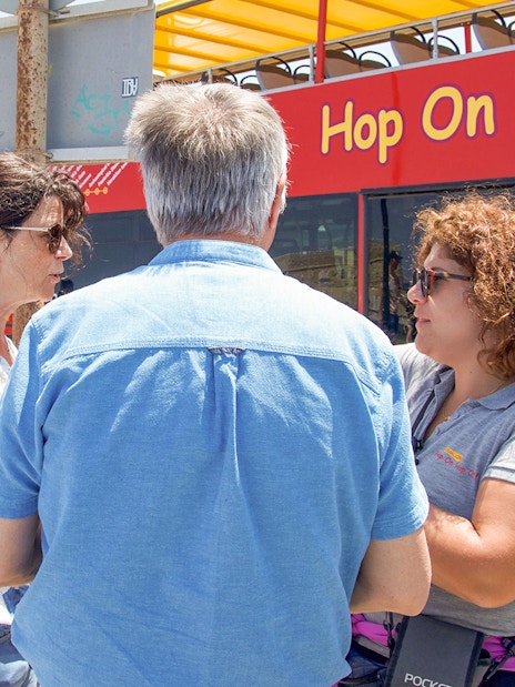 Heraklion tourists discussing with guide near Hop-On Hop-Off bus.