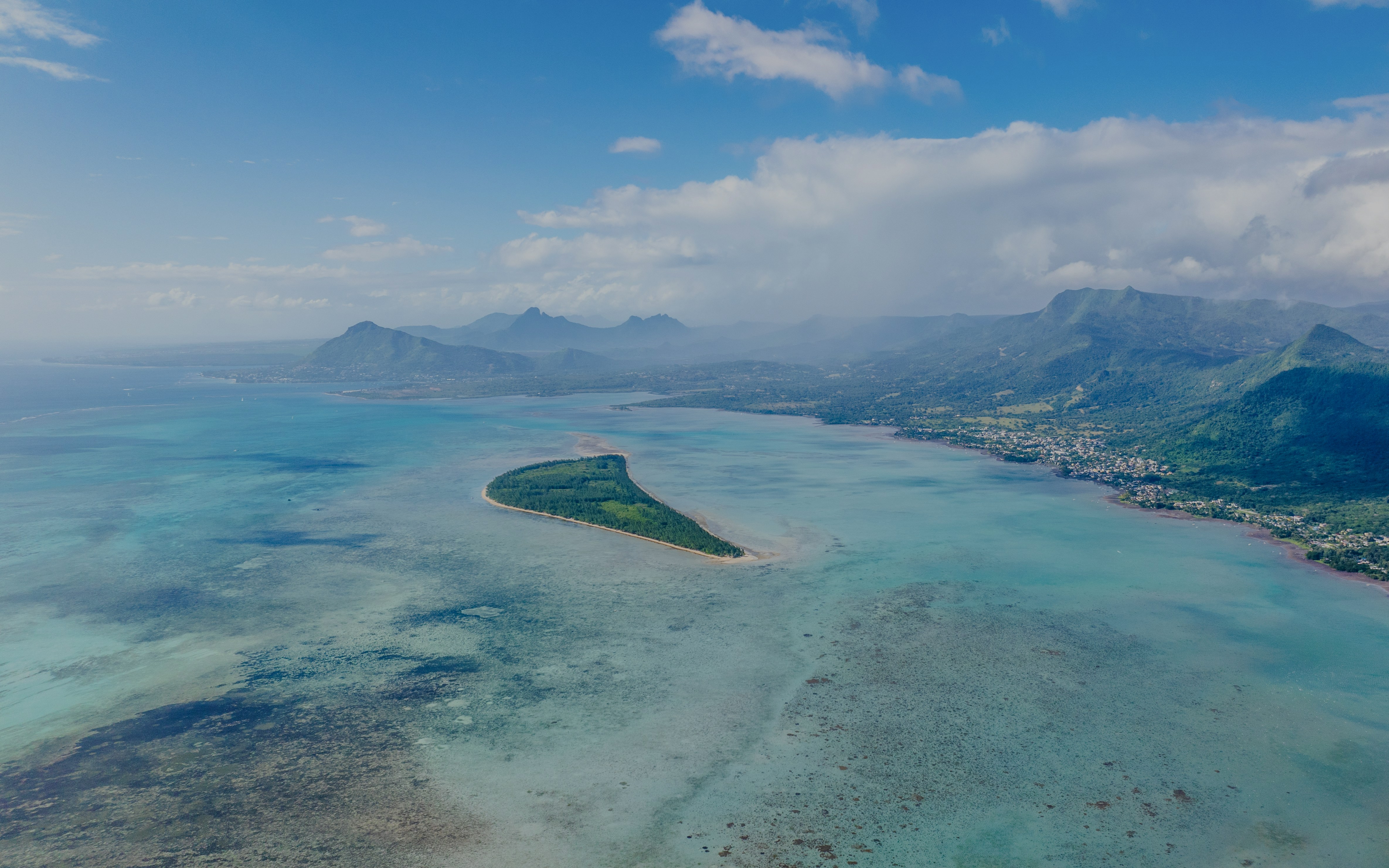 Aerial view of Île aux Bénitiers surrounded by turquoise waters and distant mountains in Mauritius.