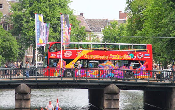 City Sightseeing Amsterdam bus crossing a canal bridge with colorful designs.