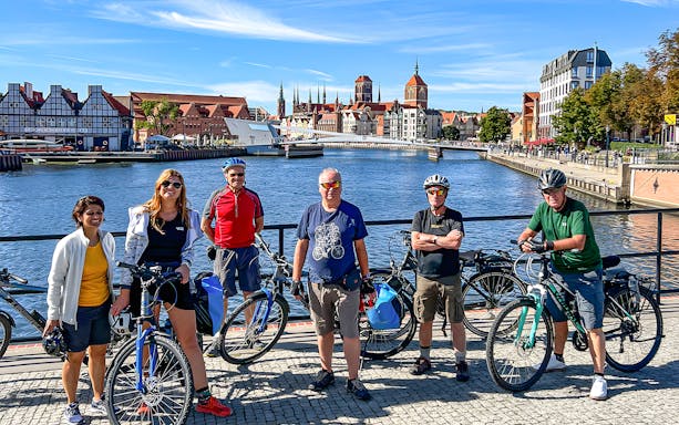 Group of cyclists on a bridge in Gdansk with historic buildings in the background.