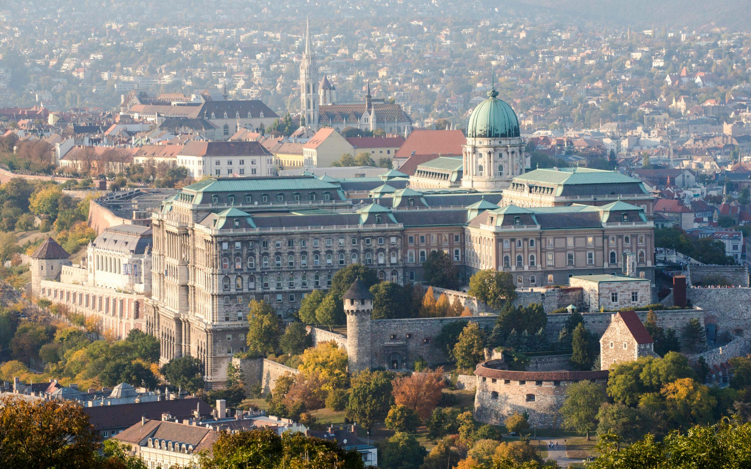 Buda Castle in Budapest with surrounding cityscape and autumn foliage.