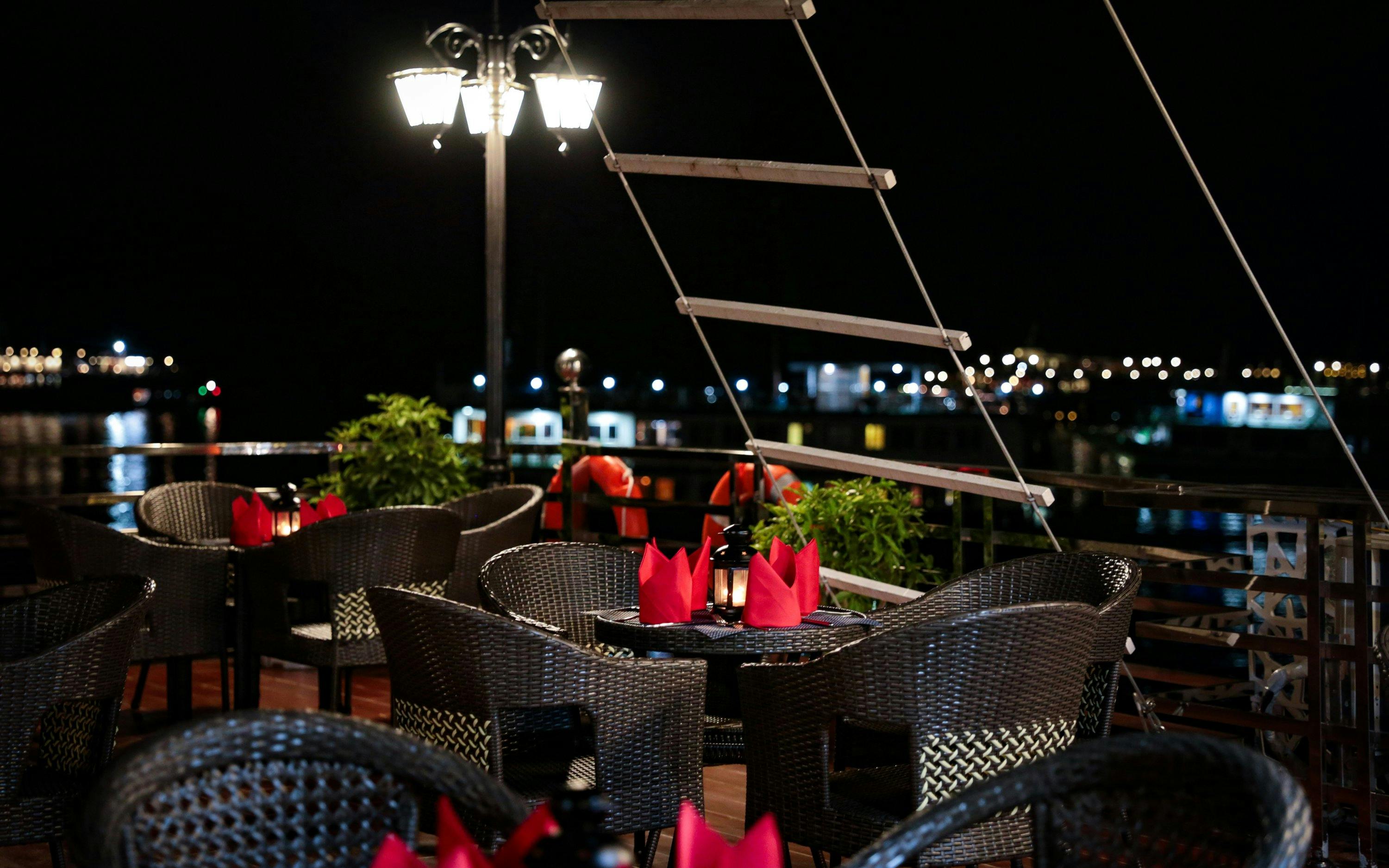 Outdoor dining area on a Lan Ha Bay cruise ship at night with lit lanterns and water view.
