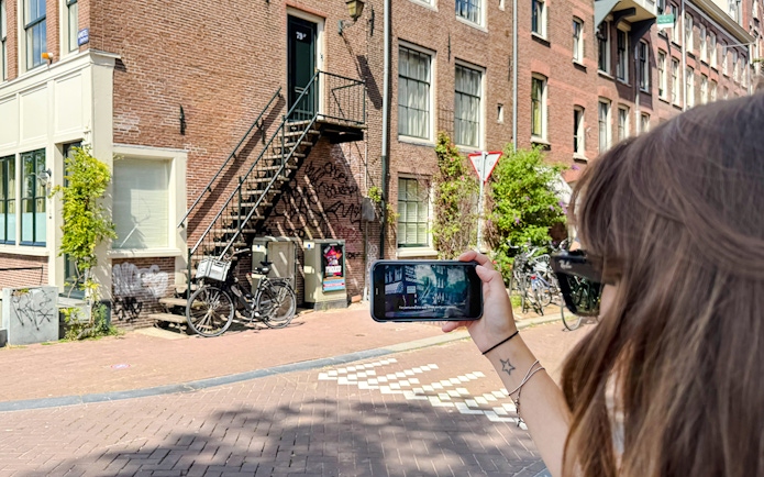 Guest using mobile guide on Anne Frank tour in Amsterdam street.