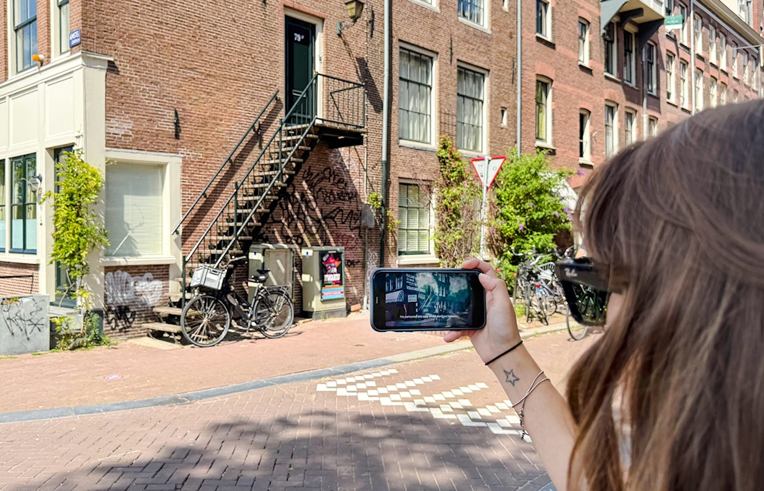 Guest using mobile guide on Anne Frank tour in Amsterdam street.