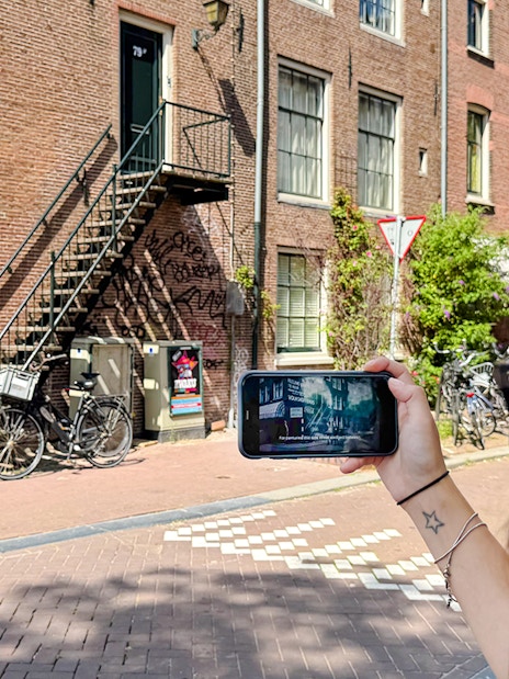 Guest using mobile guide on Anne Frank tour in Amsterdam street.