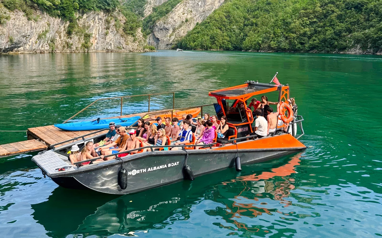 Guests on a boat tour at Komani Lake, Albania, surrounded by lush green hills.