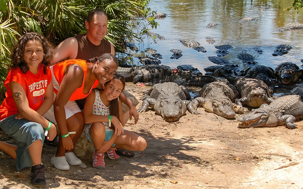Group posing near alligators at Gatorland with Screamin’ Gator Zip Line in background.