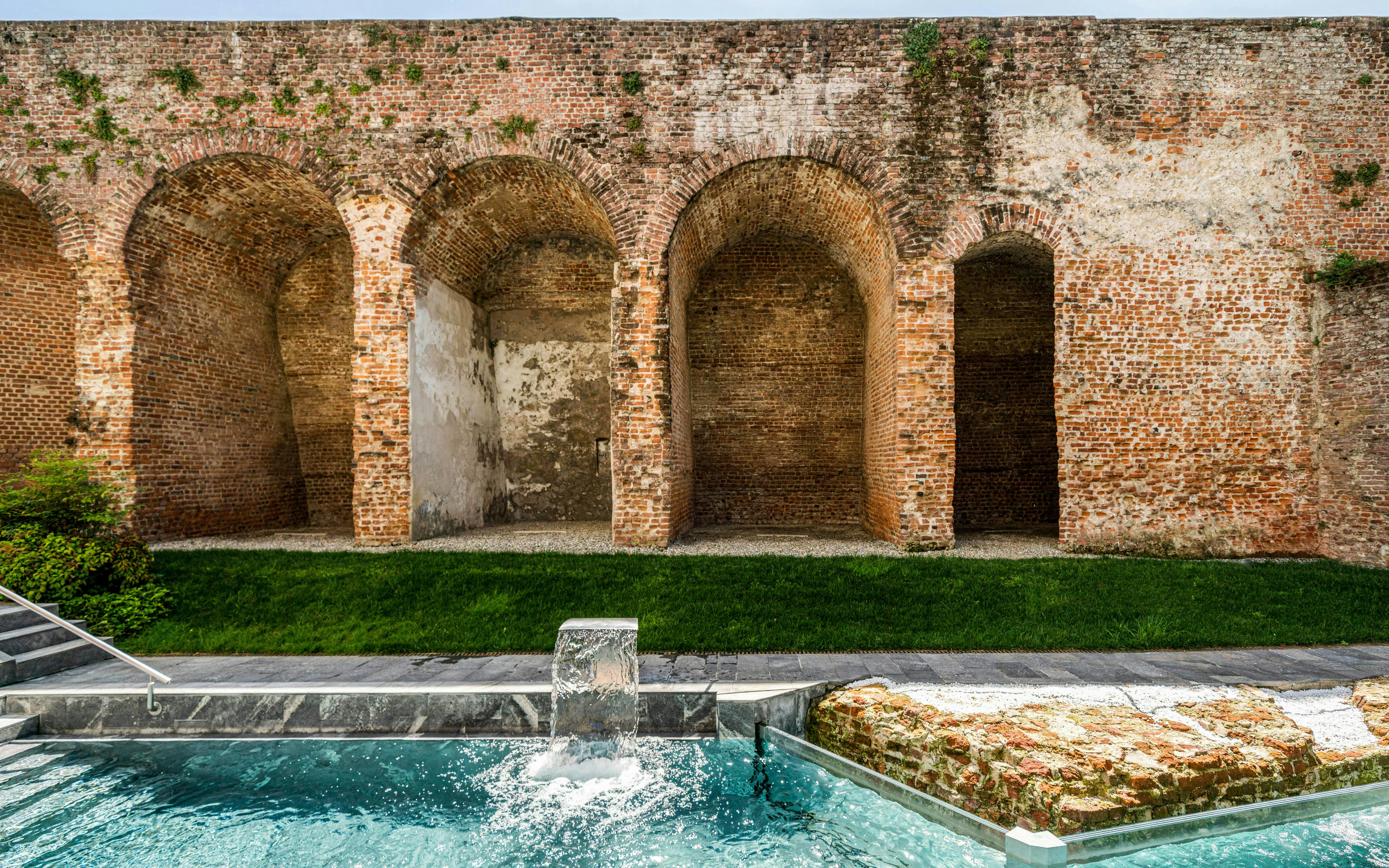 Outdoor pool with waterfall at QC Terme Milan, bordered by historic brick arches.